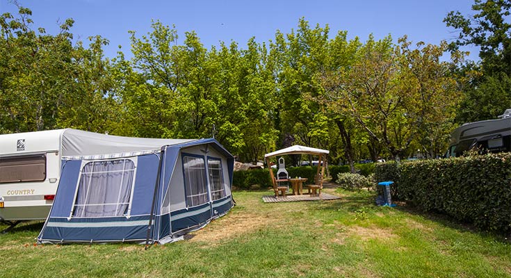 caravane, auvents et salon de jardin sur un emplacement avec barbecue